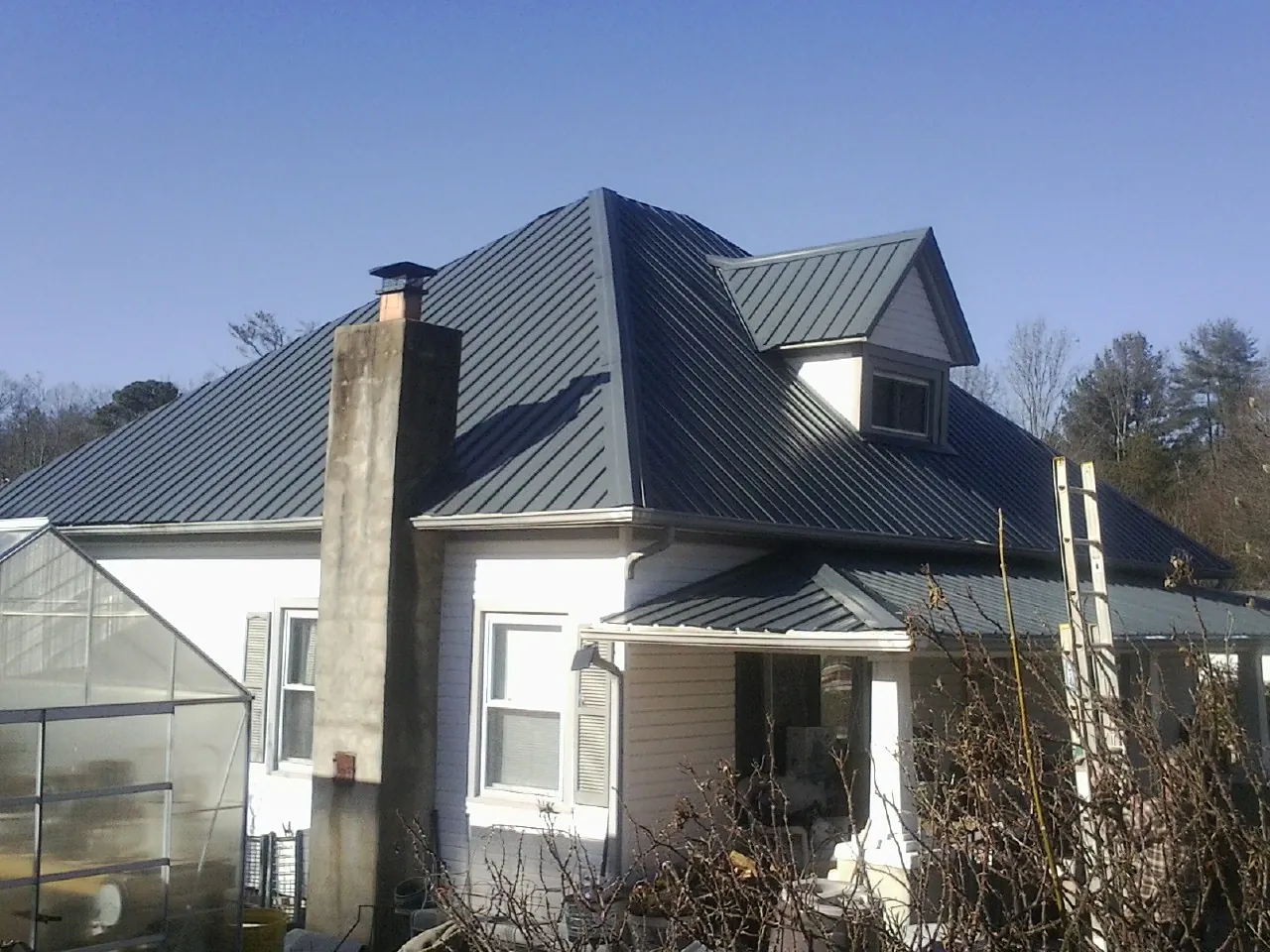 Dark blue standing seam metal roof on a white farmhouse with dormer — Slate & Tile Roof Repair by Roofing Brothers in Hazel Park