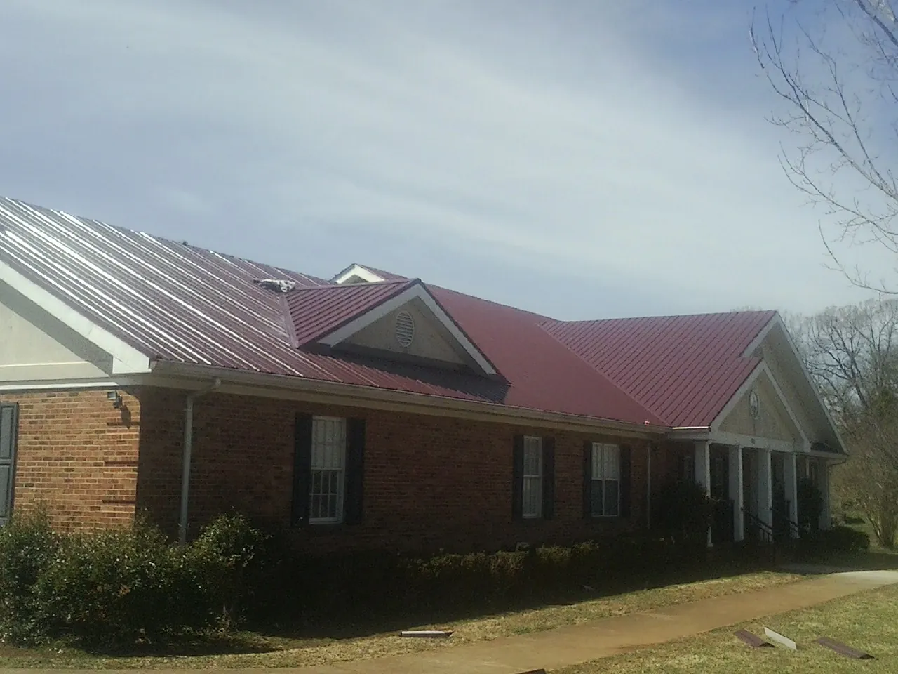 Red metal roof with gabled entries on a long brick building, from a Hail Damage Roof Repair job in Hazel Park