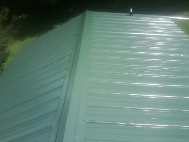 New green metal panels meeting at the ridge of a roof — Flat Roof Repair work by our crew in Hazel Park