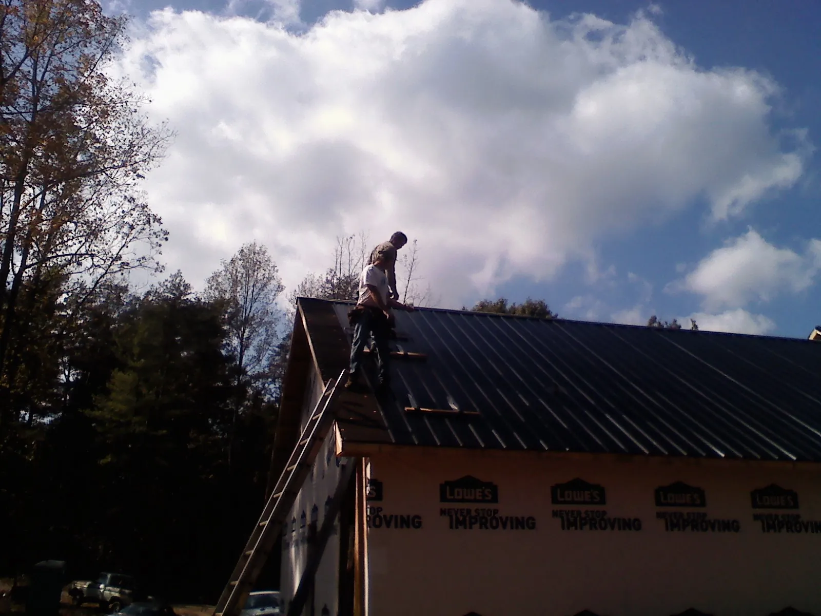 Roofer fastening dark metal panels high against a cloudy sky in Hazel Park