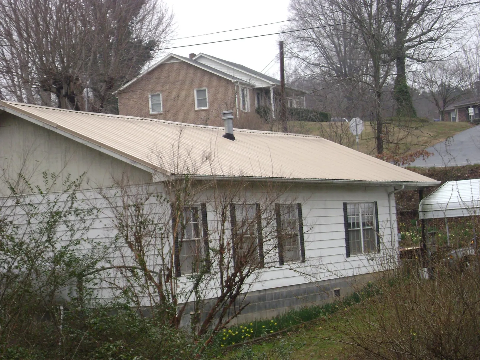 Tan metal roof on a white sided house set into a hillside — Commercial Roofing by Roofing Brothers in Hazel Park